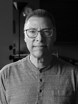 Black and white head shot of Jonathan Bloy. The right side of the photo is mostly in shadow with light coming from the left.